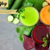 Three glasses of healthy vegetable juice with scattered ingredients, above view over a slate background